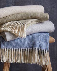 three blankets stacked on top of each other in front of a wooden stool against a wall