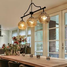 a wooden table topped with vases filled with flowers next to two lamps hanging from the ceiling