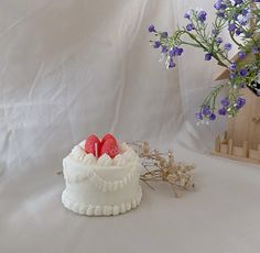 a cake with two hearts on it sitting next to a vase filled with purple flowers