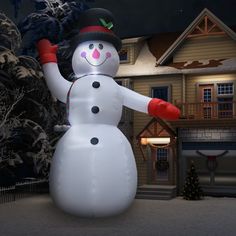 a large snowman standing in front of a house at night with its arms outstretched