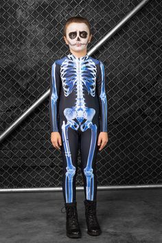 a young boy in a skeleton suit standing next to a chain link fence with his hands on his hips