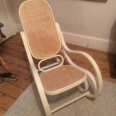 a white rocking chair sitting on top of a hard wood floor next to a wall