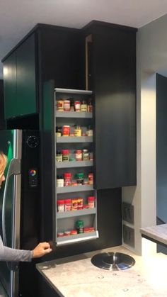 a woman is pointing at the refrigerator in her kitchen with black cabinets and white countertops