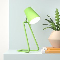 a green lamp sitting on top of a white shelf next to a potted plant