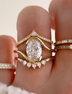 a woman's hand with three different rings on top of her finger and the ring has an oval shaped diamond surrounded by smaller diamonds