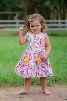 The Piper Dess is the perfect warm weather party frock with it bright floral fabric and yellow ruffle detail.  It is made of a 100% cotton and is fully lined.  Its fun flower buttons will delight your little one. Playful Floral Spring Dress, Playful Floral Print Summer Dress, Playful Summer Floral Dress, Playful Ruffled Floral Dress For Spring, Playful Spring Twirl Dress For Playdate, Playful Floral Sundress For Summer, Playful Floral Print Sundress For Summer, Spring Floral Print Sundress For Playdate, Playful Floral Print Dress For Garden Party