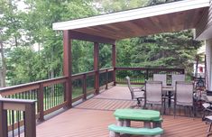 a wooden deck with chairs and tables on it, surrounded by trees in the background