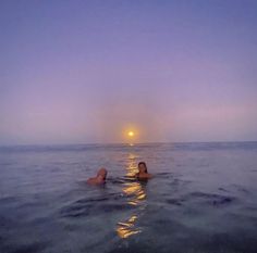 two people are swimming in the ocean at sunset or dawn with their backs turned to the camera