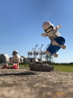 two toy figurines sitting on top of a cement ground next to each other