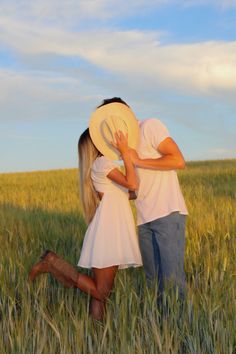 a man and woman kissing in the middle of a wheat field with a hat on their head