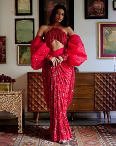 Step into iconic glamour where elegance is draped in the shimmer of scarlet palette for the season’s soirees. Our new-age concept of pre-draped saree features a chic halter neck blouse adorned with nalki crystals embellishment paired up with a sequined pre-draped skirt. Adding a hint of drama the handmade puffer sleeves complete the whole iconic look. • Pre-draped sequined skirt.• Halter-neck blouse adorned with nalki crystals and moti embellishments. • Metal hook at the back side of the blouse to conceal. • Puffed sleeves with an attached sequined dupatta.• Metal zip on the backside of the skirt along with a hook for support.From Moledro’s Fitoor collection. DELIVERY TIMEPlease allow 8-12 weeks for your outfit to arrive. FABRIC DETAILSBlouse: Butterfly Net Skirt: GeorgetteSleeves: Net Pro Elegant Pre-draped Saree For Party Season, Evening Party Wear Pre-draped Floor-length Saree, Glamorous Fitted Pre-draped Saree For Gala, Festive Fitted Pre-draped Saree For Gala, Glamorous Festive Pre-draped Saree For Gala, Festive Party Wear Blouse With Draped Sleeves, Glamorous Lehenga For Gala Festivities, Festive Party Wear Saree With Draped Sleeves, Glamorous Lehenga For Festive Gala