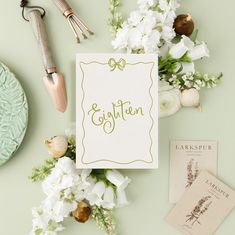 a table topped with flowers and cards next to utensils on top of a green surface