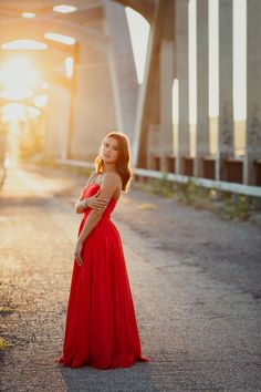 a woman in a red dress standing on the side of a road with her arms crossed