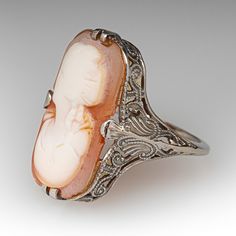 This antique filigree cameo ring features an elongated shell cameo of a woman's bust. The ring was loved and worn over the years and the cameo bust is a bit worn. The ring itself has crisp and strong details with open scroll work and milgrain. The ring is crafted in 10k white gold and is currently a size 5. The cameo is glued in for security. Antique Cameo Ring Collectible, Art Deco Cameo Ring For Collectors, Art Deco Cameo Ring Collectible, Art Deco Cameo Collectible Rings, Vintage Oval Cameo Ring, Vintage Cameo Rings For Collectors, Vintage Cameo Rings For Wedding, Formal Oval Carved Filigree Ring, Collectible Art Deco Cameo Jewelry