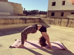 a woman in black shirt doing yoga on pink mat with buildings in the back ground