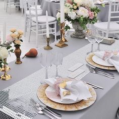 the table is set with white and gold plates, silverware, and pink flowers