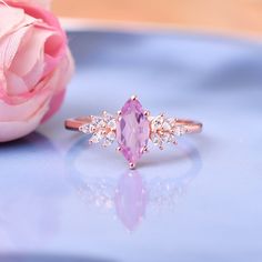 a pink rose sitting on top of a table next to a ring with an oval shaped stone