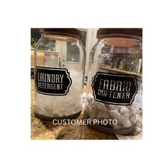 two glass jars with labels on them sitting on a counter top next to each other