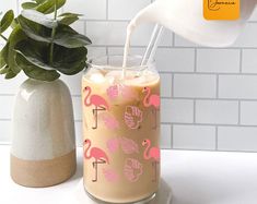 a drink being poured into a glass with pink flamingos on it and a potted plant in the background