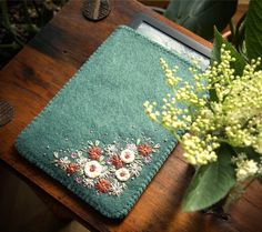 a green case with flowers on it sitting next to a flower arrangement and a laptop