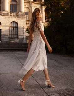 a woman is walking in front of an old building wearing high heels and a white dress