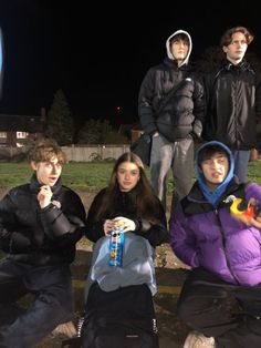 four people sitting on the ground posing for a photo at night with one person holding an object in front of them