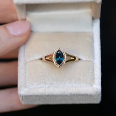 a woman's hand holding an open ring with a blue stone in it