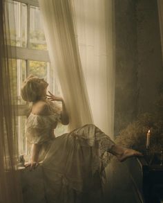 a woman sitting on a window sill next to a candle