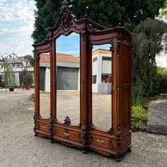 a large wooden armoire sitting on top of a cobblestone street next to a tree