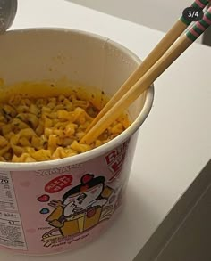 a bowl of noodles with chopsticks in it on a counter top next to a measuring spoon