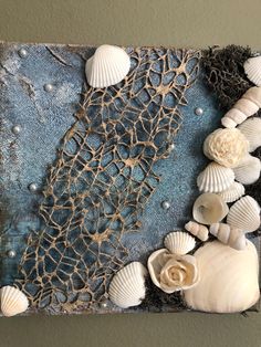 some sea shells and other things are on a piece of art that is hanging on the wall