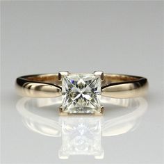 an engagement ring with a princess cut diamond in the center on a reflective surface,