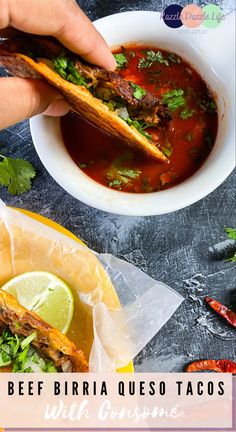 someone holding a taco in their hand over a bowl of soup with limes and cilantro on the side