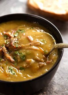 a close up of a bowl of soup with bread in the background