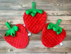 three red strawberries with green bows are on a wooden table and one is made out of felt