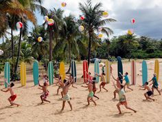 a group of people running on the beach with surfboards and balloons in the air