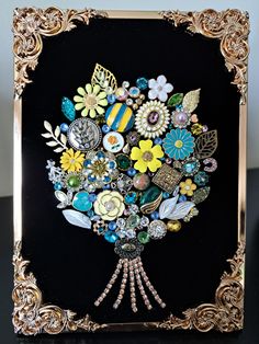 an ornate gold frame holds a bouquet of flowers and brooches on black background