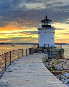 a light house sitting on top of a pier next to the ocean under a cloudy sky