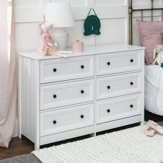 a white dresser sitting in a bedroom next to a bed with pink sheets and pillows