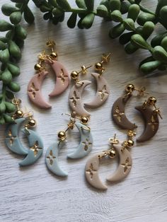 six pairs of earrings sitting on top of a table next to green leaves and flowers