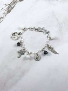 a silver bracelet with charms and an angel charm on it, sitting on a marble surface