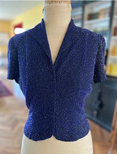 "A spectacular evening blouse/jscket made of wool crepe entirely covered in deep blue beading in a swirl pattern.  Few of these blouses survive intact but this one is in fine fine condition. Shirt sleeves, lapel collar and hooks and eye centre front closure. The pin tucks at the lower back are beautifully finished with the beads having been removed to highlight the tucks. In excellent condition  Size S-M Bust 34\" Waist 28\" Length 18\" Sleeve length 7\"" Fitted Beaded V-neck Blouse, Vintage Fitted Beaded Tops, Fitted Vintage Beaded Tops, Vintage Beaded Fitted Tops, Fitted Silk Top With Sequins, Fitted Silk Sequin Tops, Elegant Fitted Beaded Blouse, Blue Fitted Blouse For Evening, Elegant Formal Blouse With Beaded Details