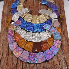 a piece of art made out of different colored glass tiles on a tree trunk with a white plate in the background