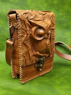 a brown leather purse with an owl design on the front and side, sitting on a green surface