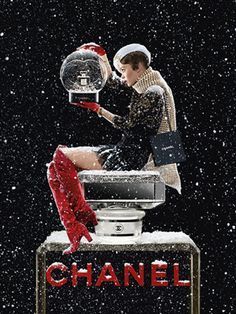 a woman is sitting on top of a chanel bottle with snow falling all over her