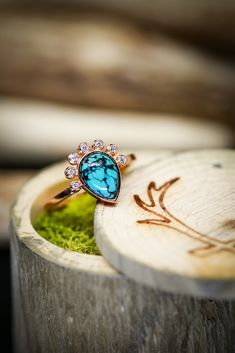 a blue ring sitting on top of a piece of wood next to a green plant