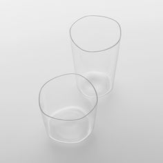 two clear glasses sitting next to each other on a white surface with no one around them