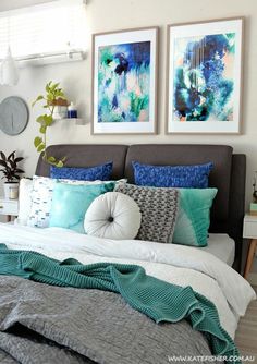 a bed with blue and white pillows in a bedroom next to pictures on the wall