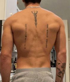 the back of a man with tattoos on his upper and lower half, standing in front of a mirror