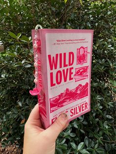 a person holding up a pink book with the title wild love on it in front of some bushes